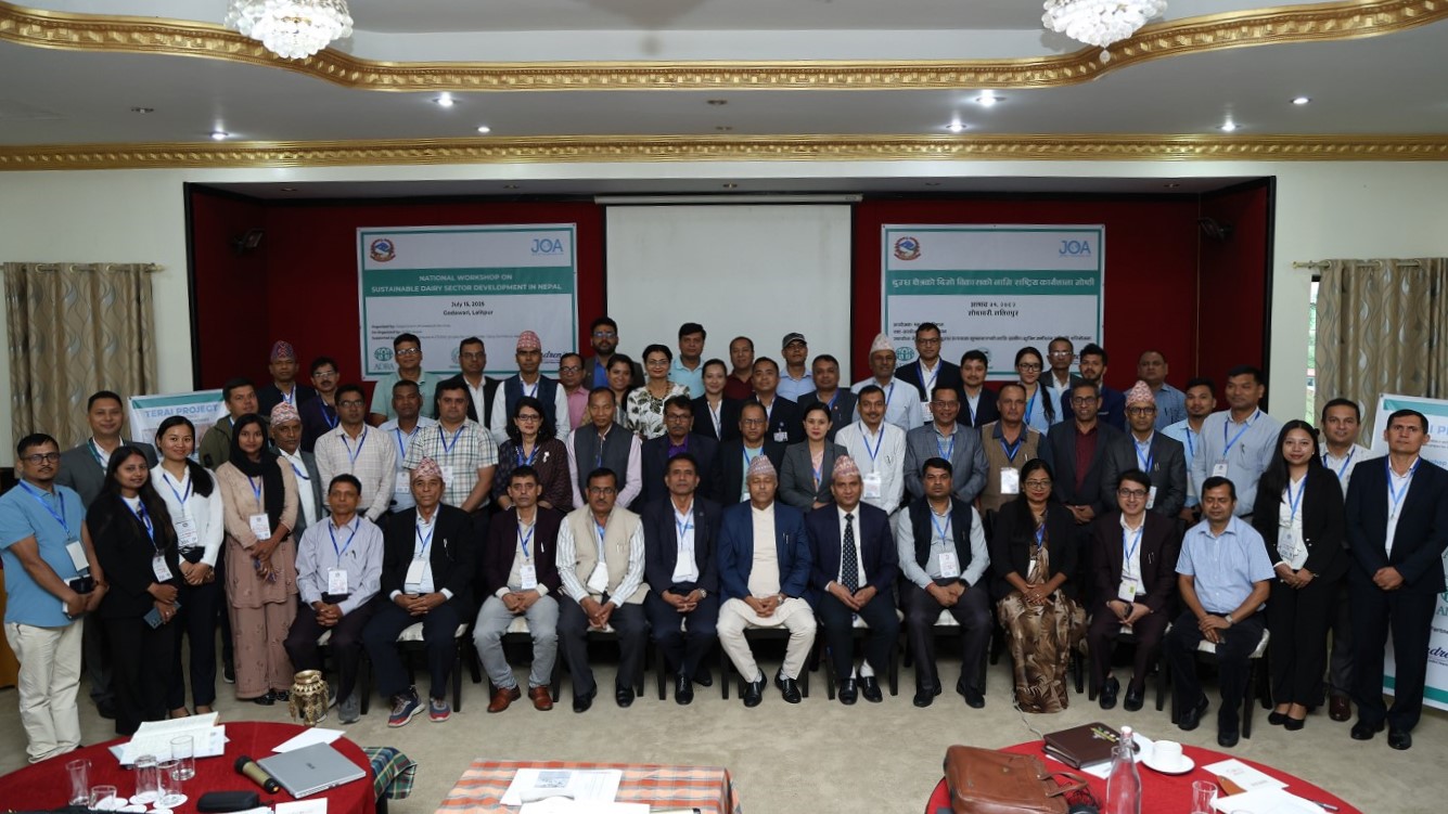 A large group of diverse individuals, including government officials, experts, and farmers, pose for a group photo in a conference room with banners in the background, at the National Workshop on Sustainable Dairy Sector Development in Nepal.