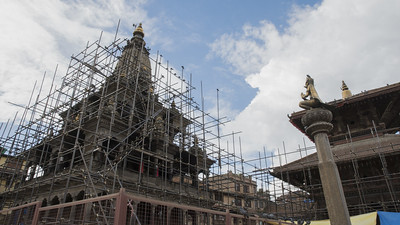 A temple in Kathmandu, Nepal, is being rebuilt with lots of scaffolding around it under a cloudy sky.