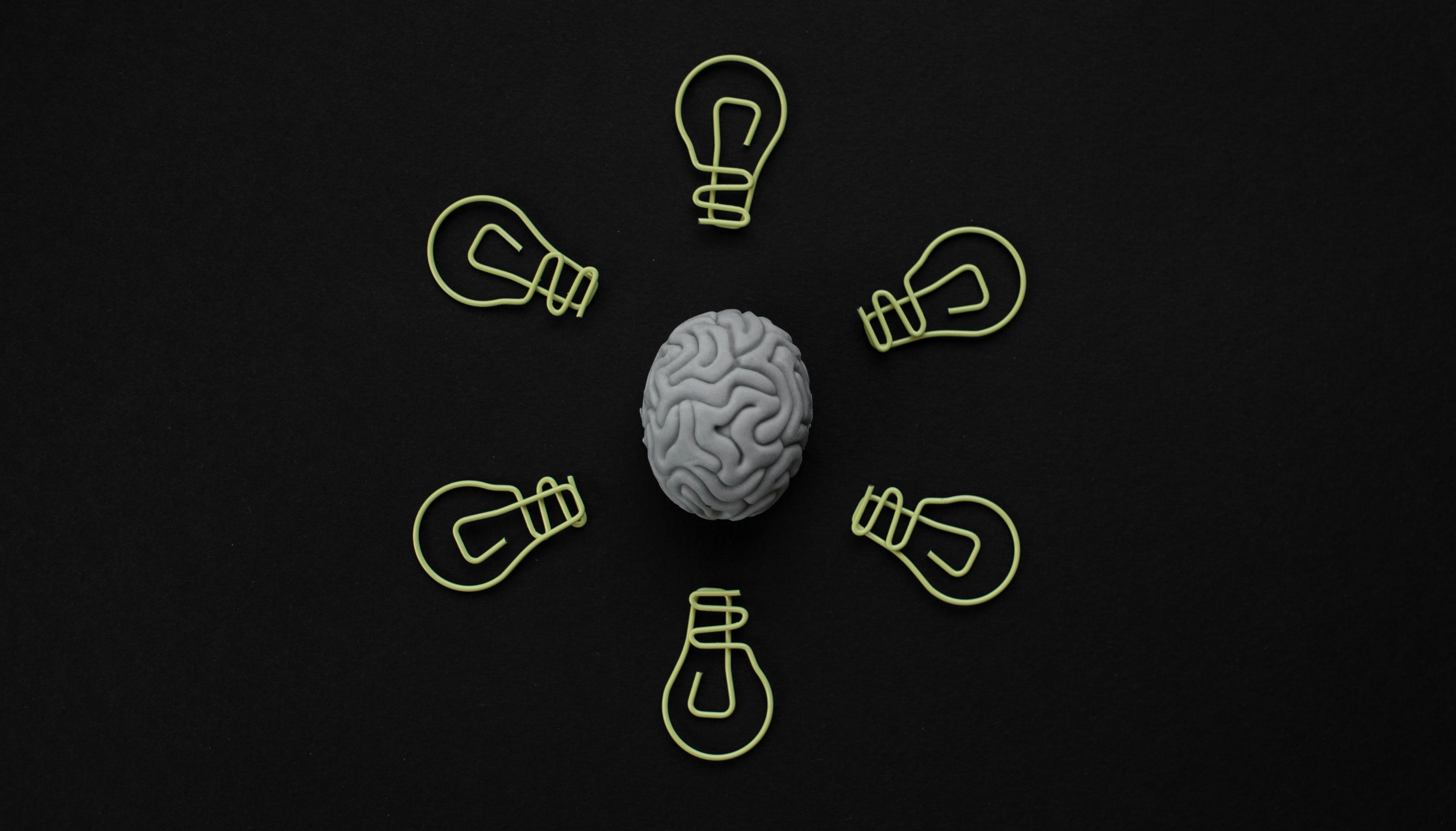 A grey brain model surrounded by seven yellow lightbulb outlines on a black background.