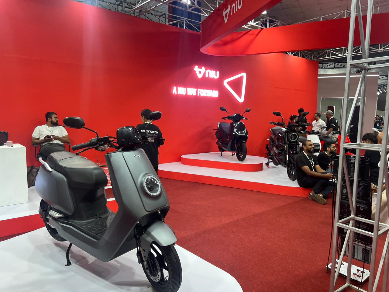 A red-themed exhibition booth showcases several NIU brand electric scooters.