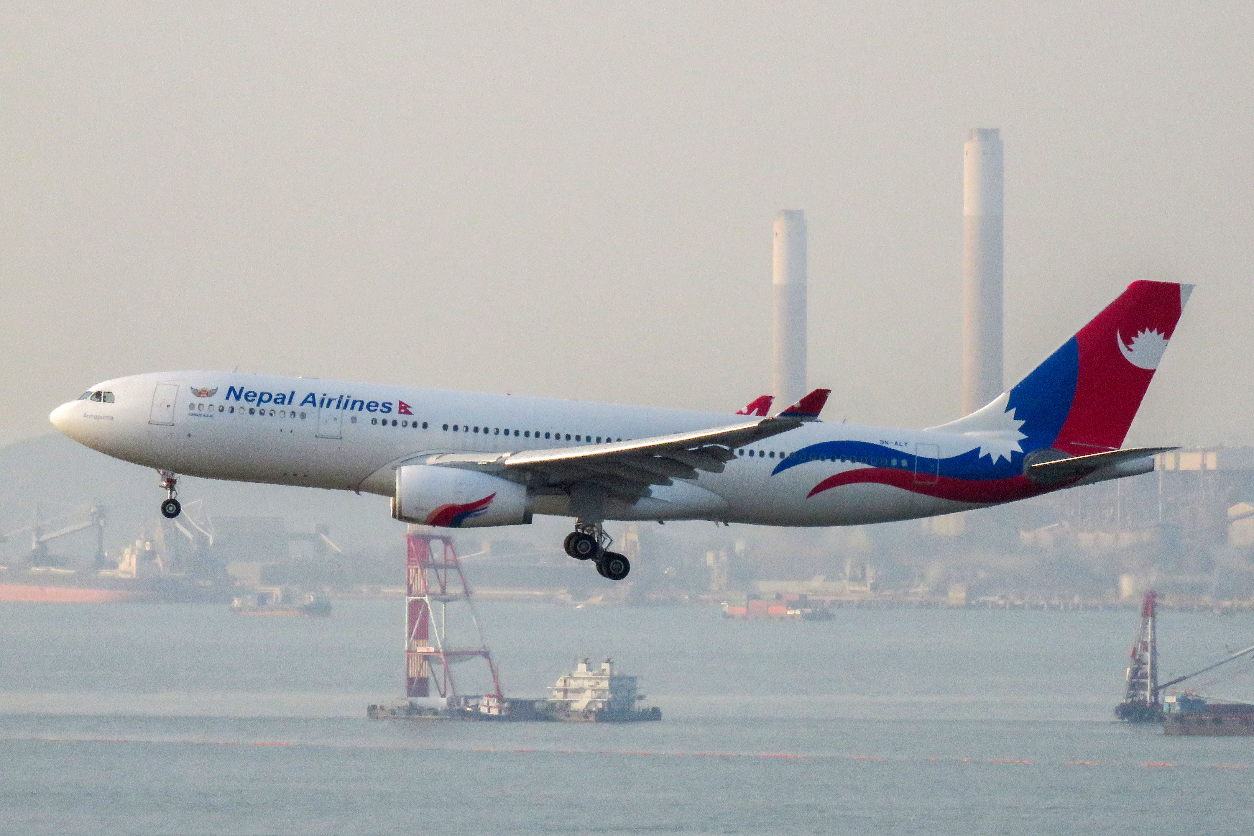 Nepal Airlines plane in flight against a clear blue sky, landing in Hong Kong